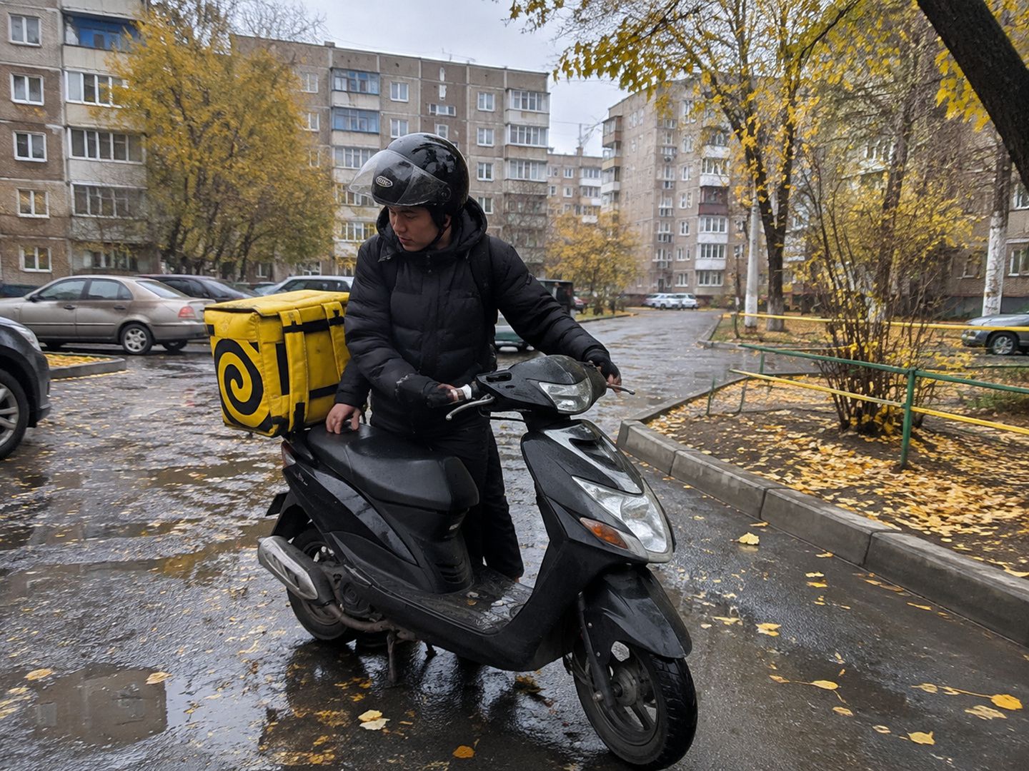Курьер Яндекс Еды паркует мопед во дворе многоэтажек в Караганде поздней осенью